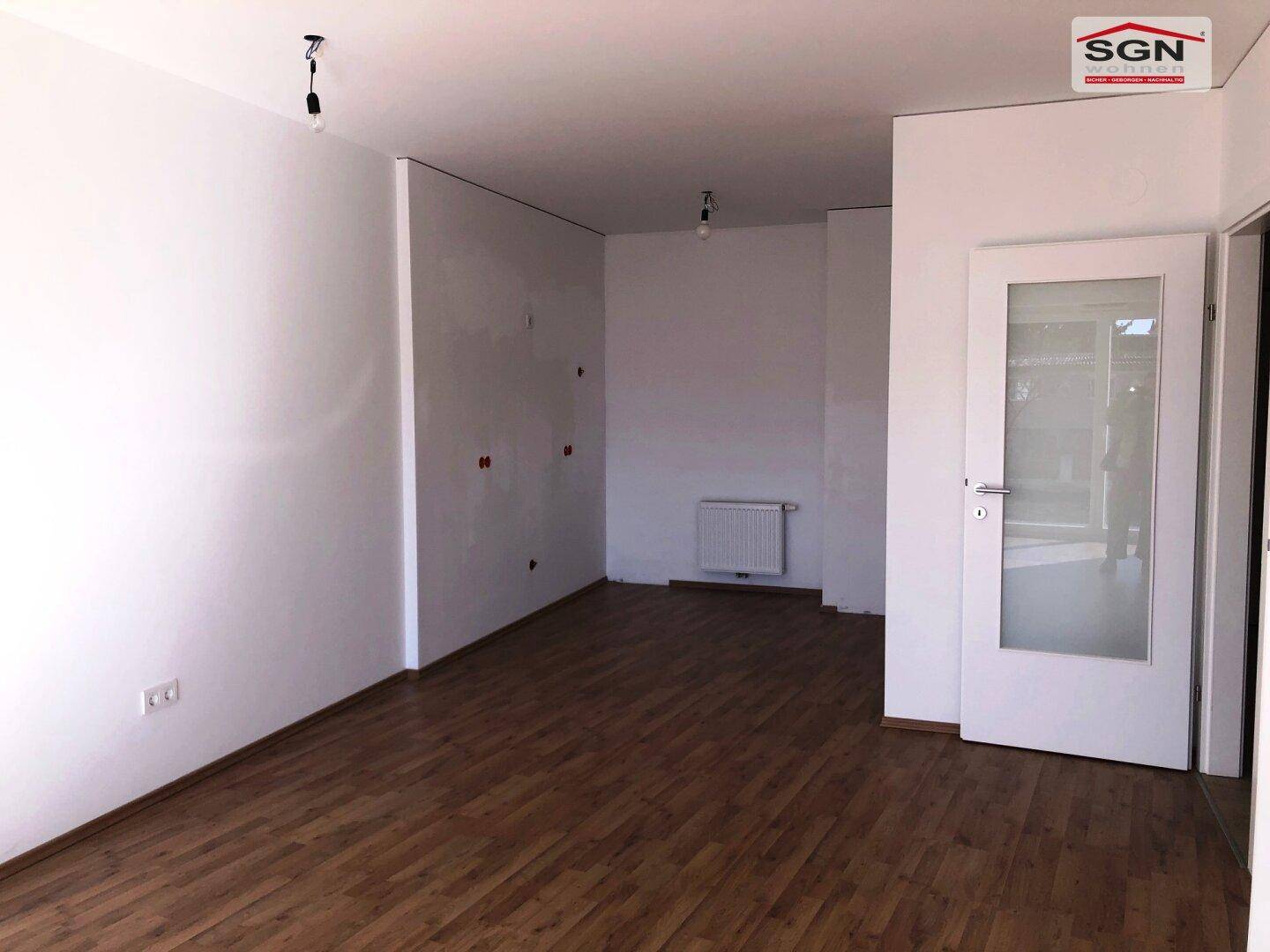 Leerer Raum mit Holzboden, weißen Wänden und Heizkörper, bereit zur individuellen Gestaltung.