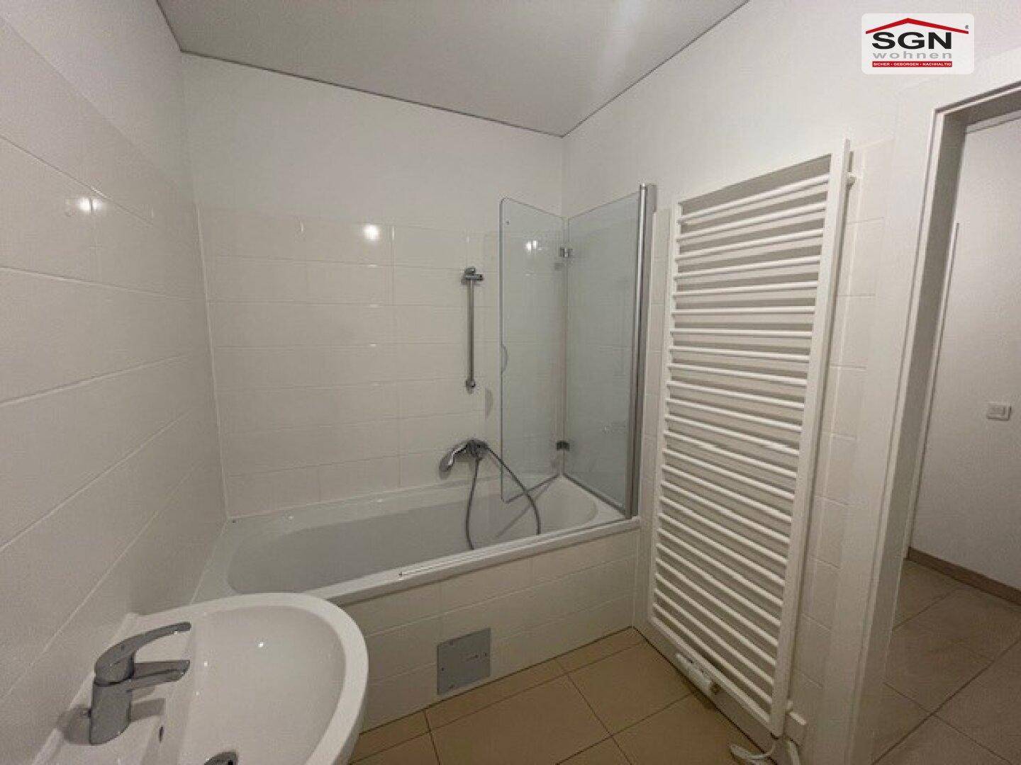 Badezimmer mit Badewanne, Duschabtrennung und beheiztem Handtuchhalter in neutralen Farben.