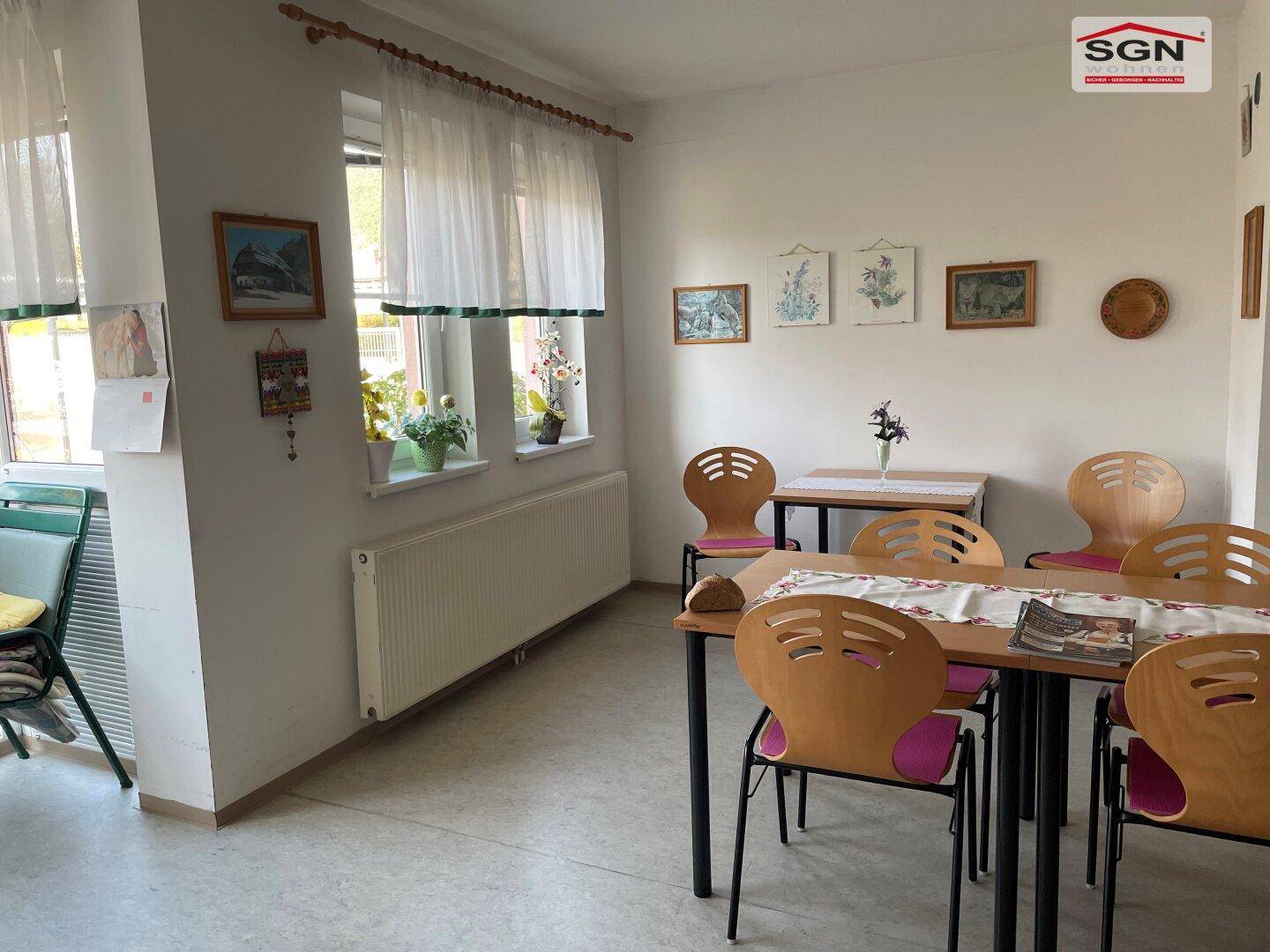 Heller Essbereich mit mehreren Tischen und Stühlen, dekoriert mit Bildern an der Wand.