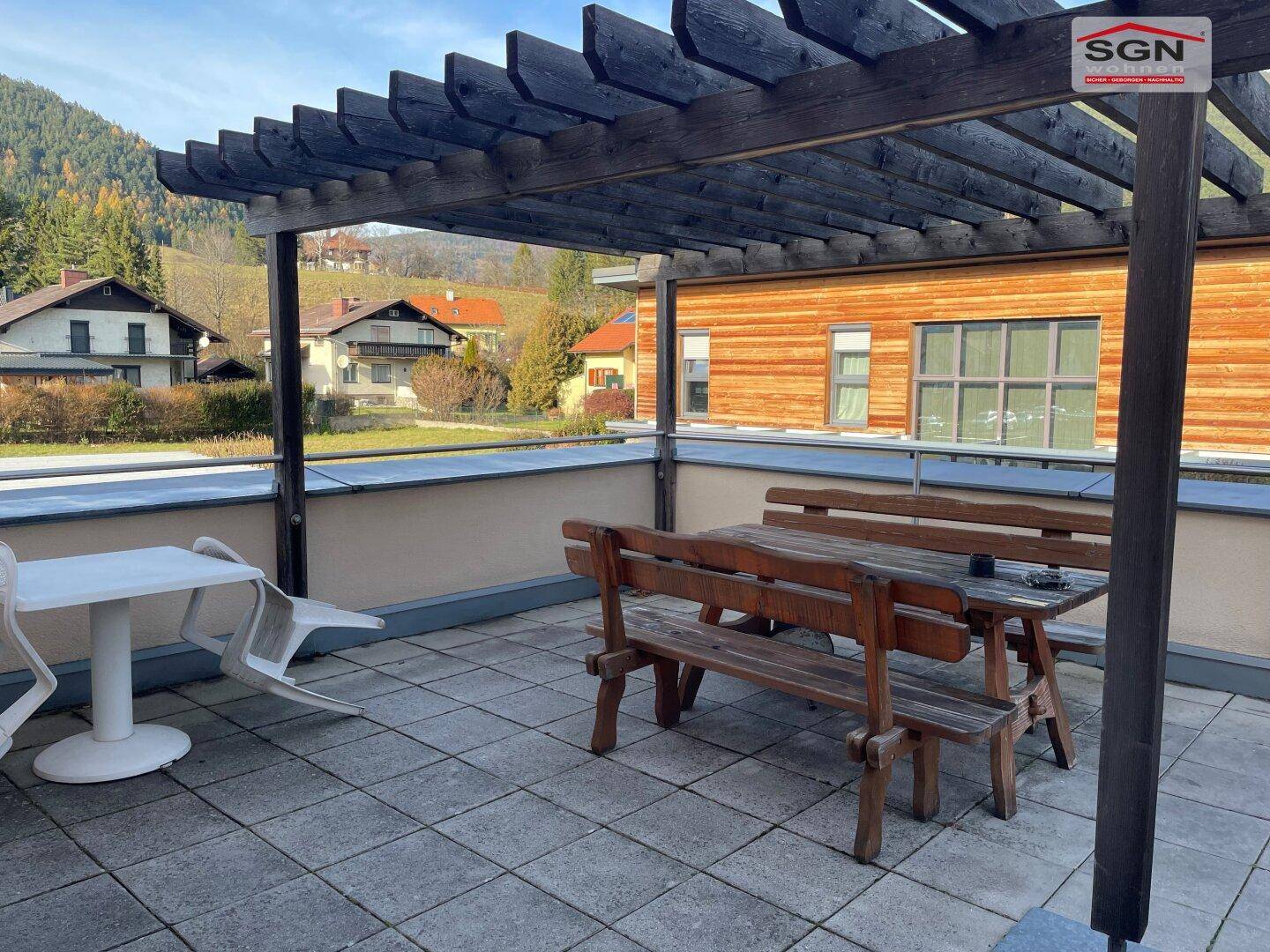 Geräumige Terrasse mit Holzpergola und rustikalen Sitzgelegenheiten, umgeben von grüner Landschaft.