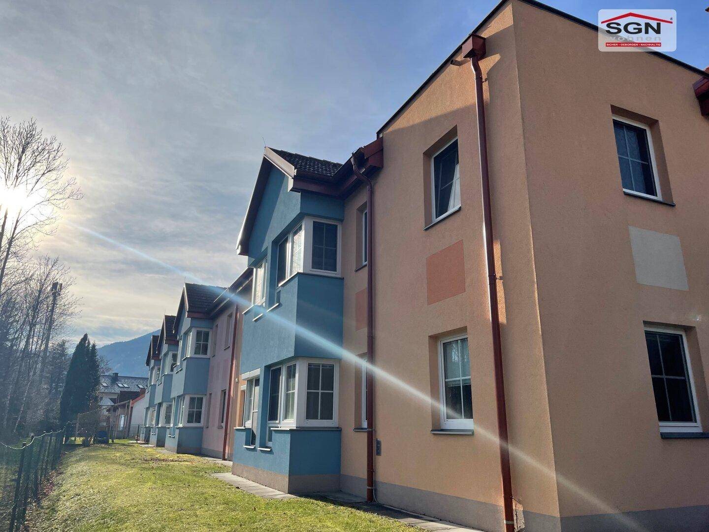 Reihe von modernen Gebäuden mit farbigen Fassaden und großen Fenstern unter strahlendem Himmel.