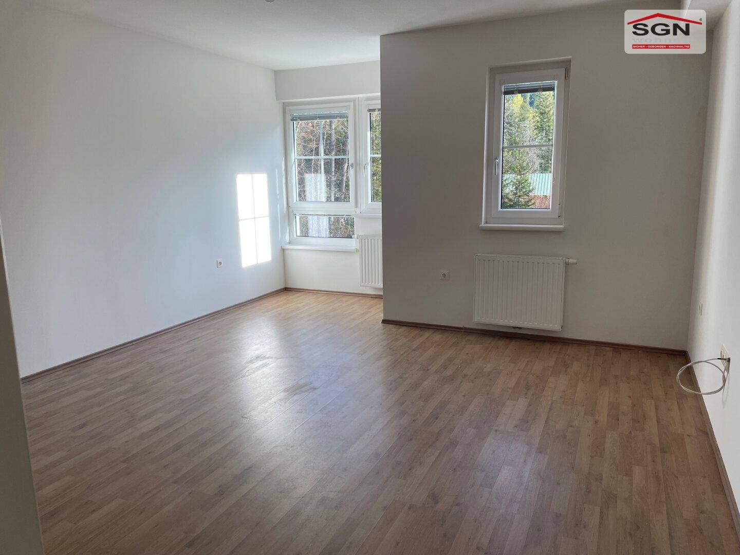 Geräumiger, leerer Wohnbereich mit hellem Holzboden und großen Fenstern für viel Licht.