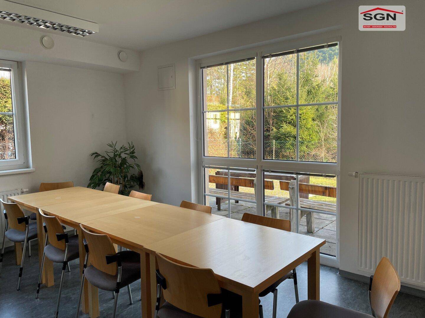 Großer Ess- oder Gemeinschaftsraum mit langem Holztisch und großen Fenstern mit Blick ins Grüne.