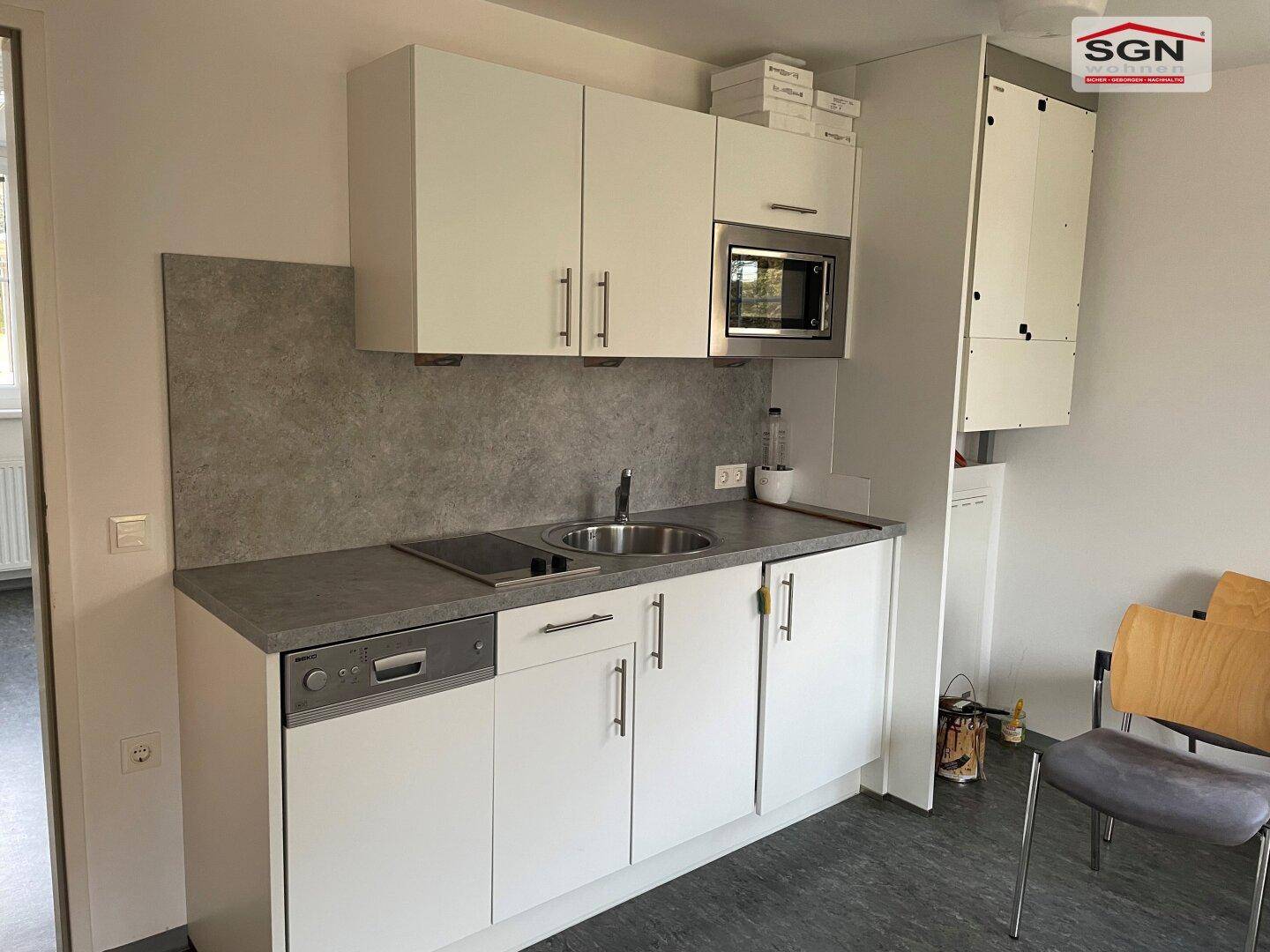 Kompakte Küchenzeile mit weißen Schränken, Spüle, Kochfeld und integrierter Mikrowelle.