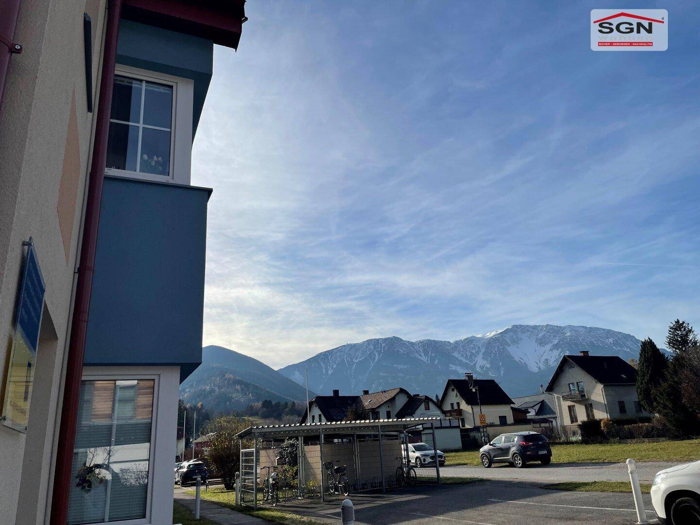 Malerischer Blick auf die schneebedeckten Berge und die umliegende Wohnsiedlung unter blauem Himmel.