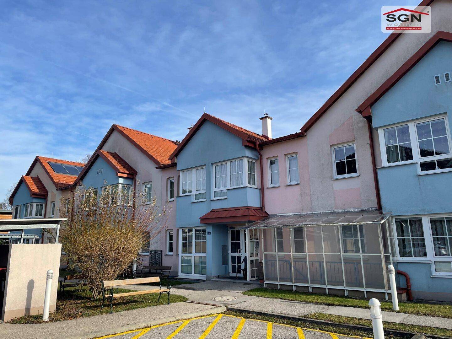 Reihe von farbenfrohen Wohngebäuden mit Satteldächern und gepflegten Vorgärten unter blauem Himmel.