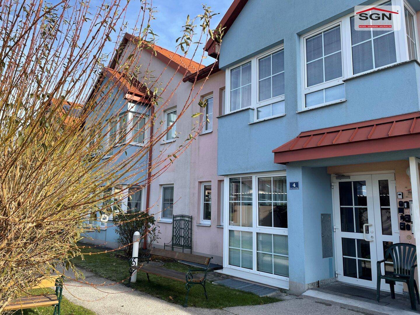 Ansicht der Wohngebäude mit farbigen Fassaden und Eingangsbereichen, umgeben von Bäumen und Grünflächen.