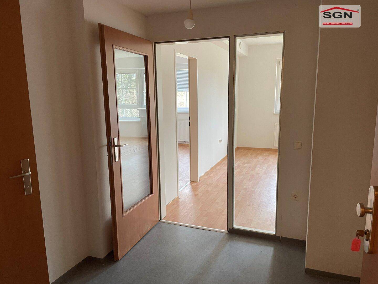 Eingangsbereich mit Fliesenboden und Holztür, der den Blick in einen weiteren Raum freigibt.