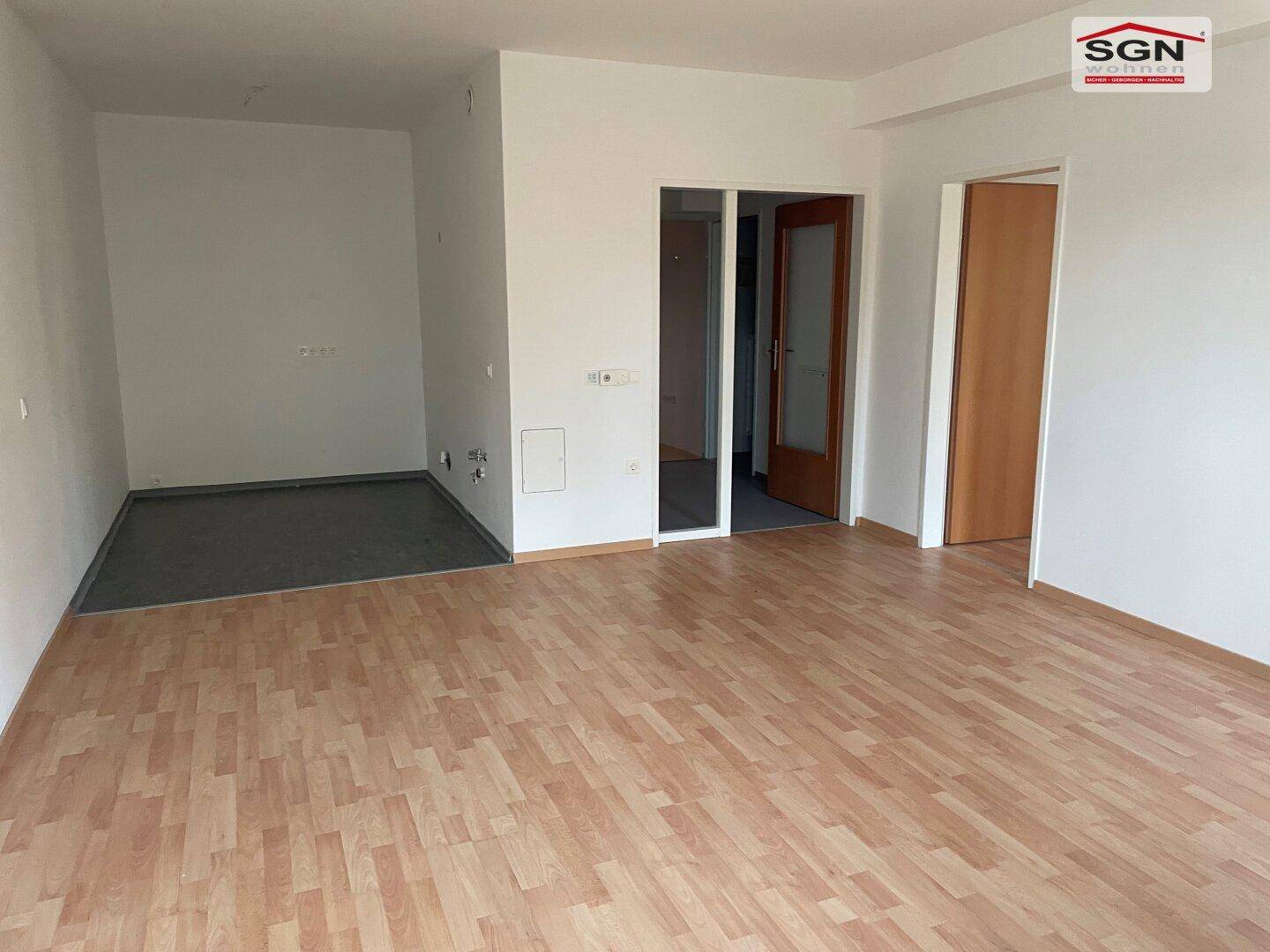 Heller, leerer Raum mit Laminatboden und einem kleinen gefliesten Bereich, bereit zur individuellen Gestaltung.