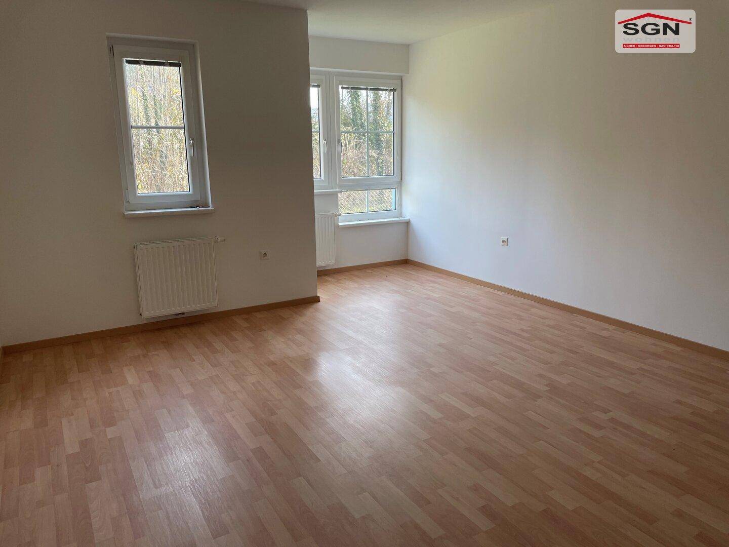Geräumiger, heller Raum mit Laminatboden und mehreren Fenstern, die viel Tageslicht bieten.