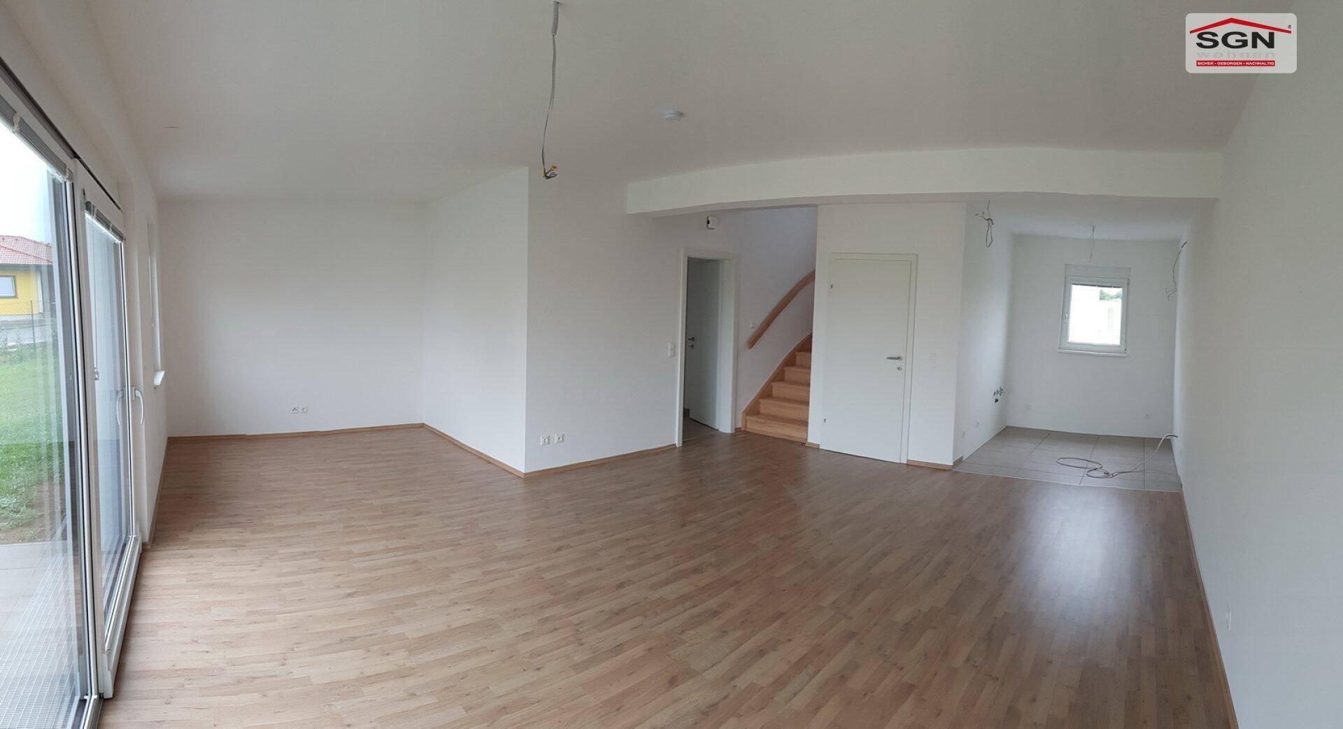 Geräumiger, heller Wohn-Essbereich mit Laminatboden und Zugang zu einer Treppe im Neubau.