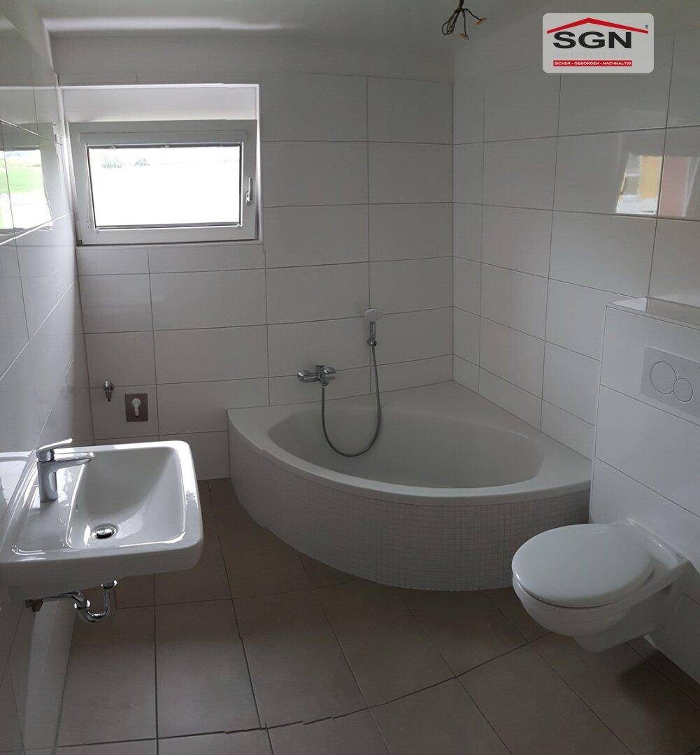 Modernes Badezimmer mit Eckbadewanne, WC, Waschbecken und Fenster in hellen Fliesen.