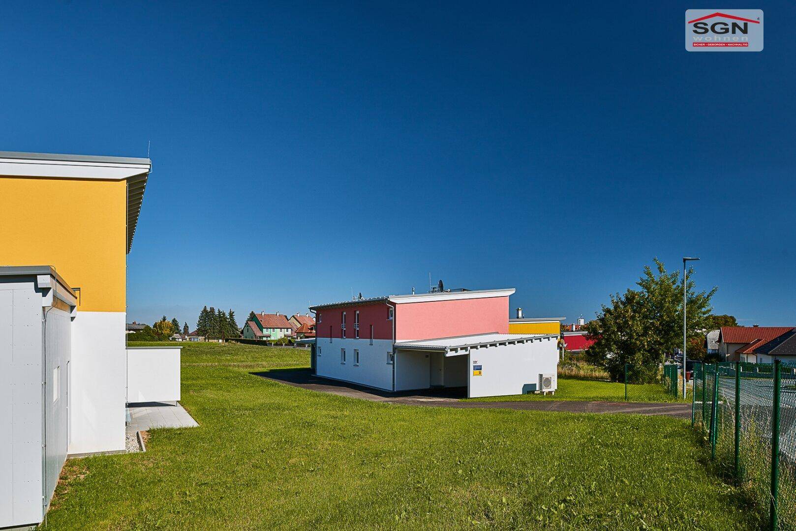 Rückansicht des Neubaus mit angrenzendem Carport und weitem Blick über die grüne Landschaft.