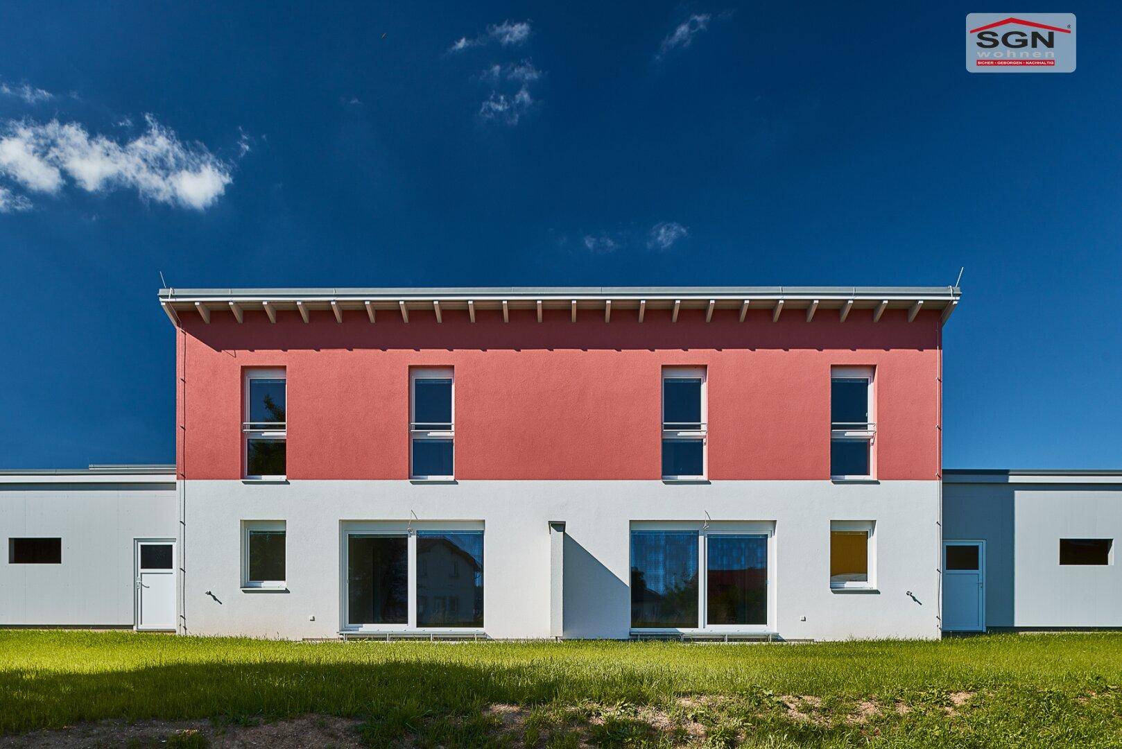 Nahaufnahme der modernen Fassade des Neubaus mit rotem Obergeschoss und weißen Fensterrahmen.