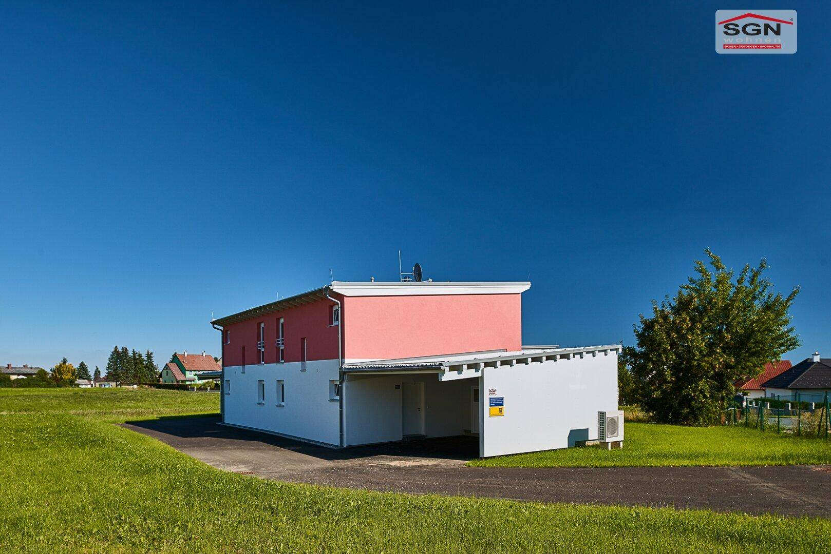 Seitenansicht des Neubaus mit integriertem Carport und Zufahrt auf asphaltiertem Untergrund.