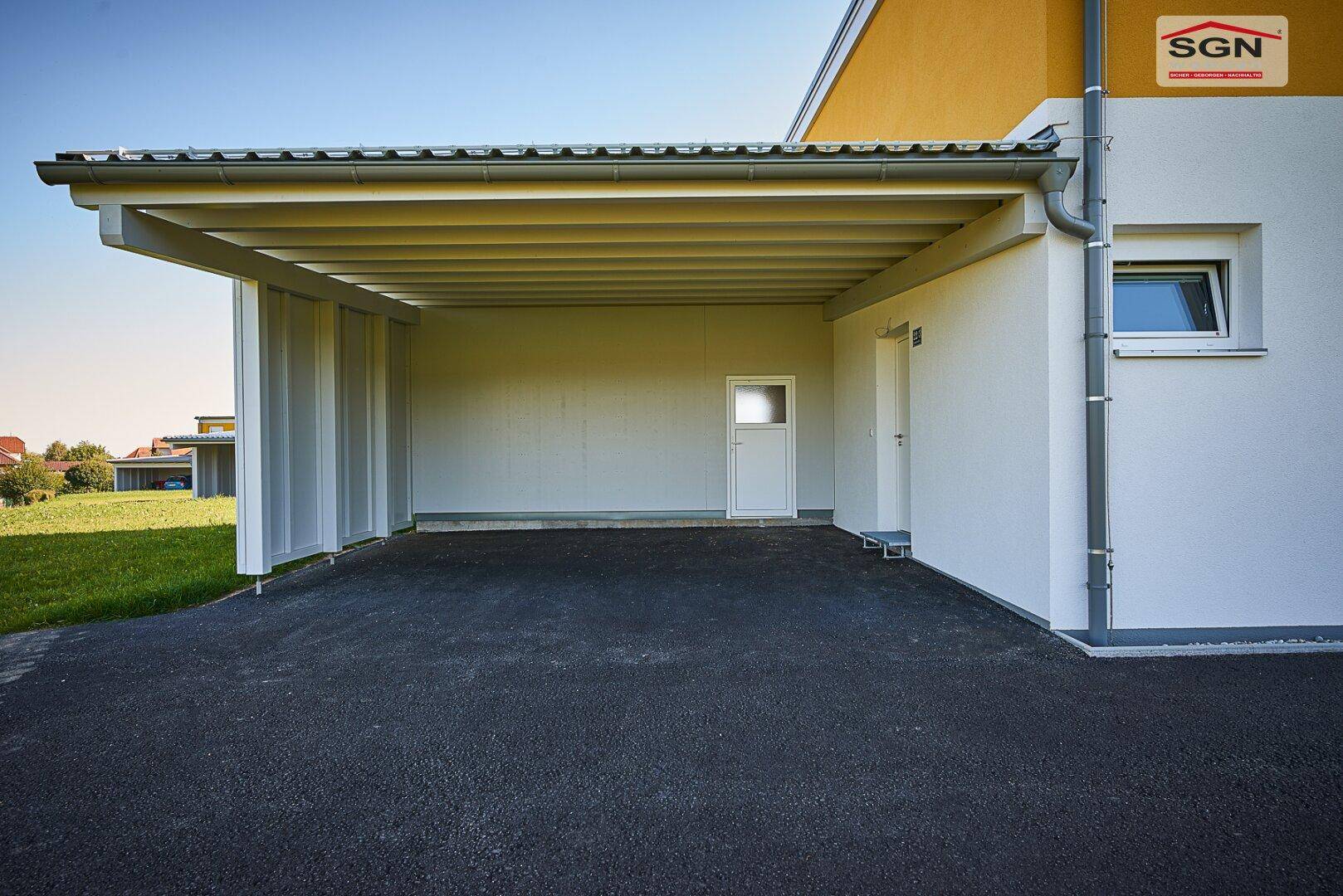 Überdachter Carport-Bereich mit asphaltiertem Boden und direktem Zugang zum Haus.