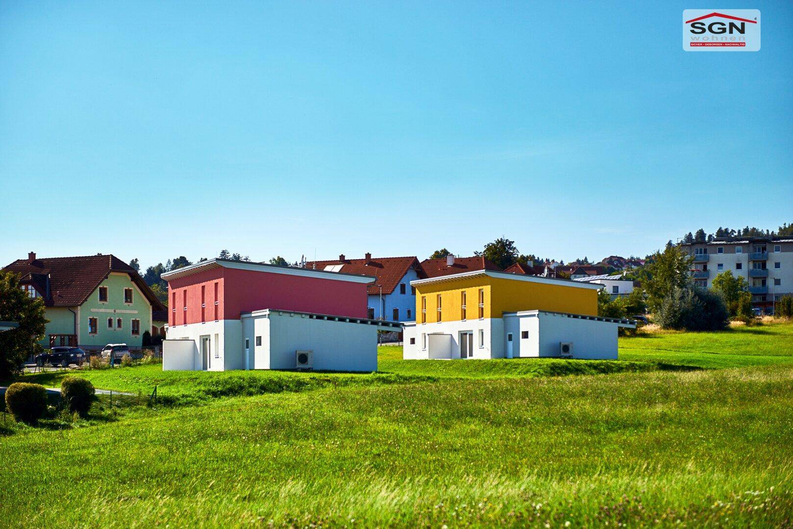Zwei moderne Einfamilienhäuser mit farbigen Fassaden in ländlicher Umgebung mit weitem Grünblick.