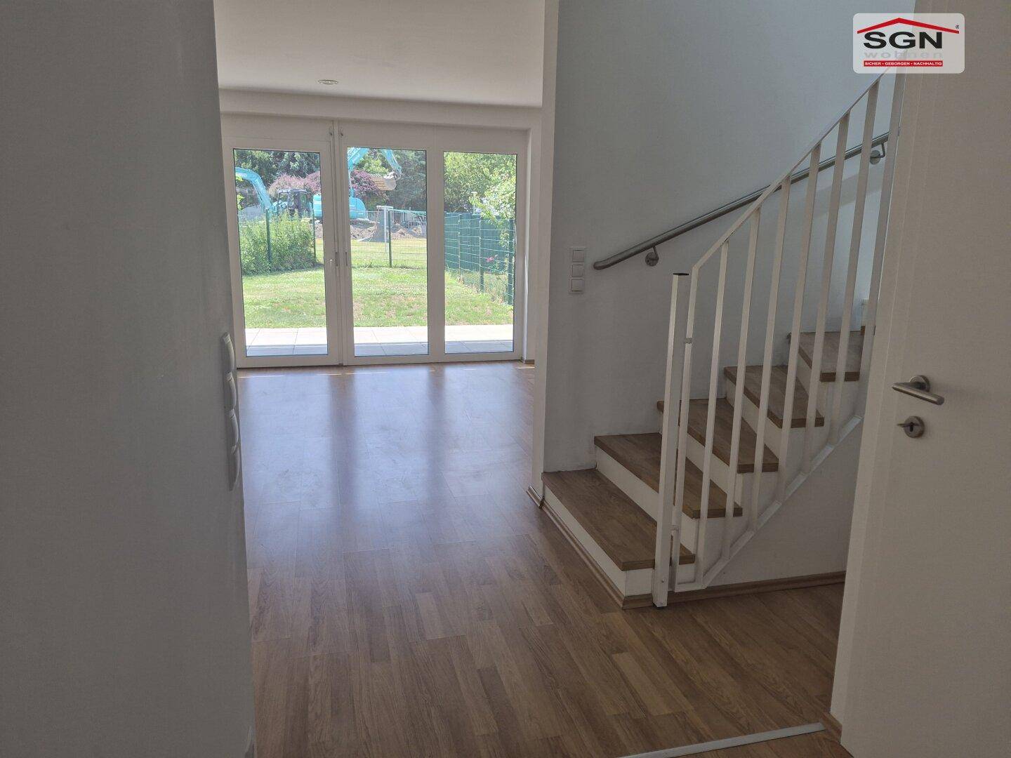 Heller Flur mit Holztreppe und Blick auf den Garten durch große Glastüren.
