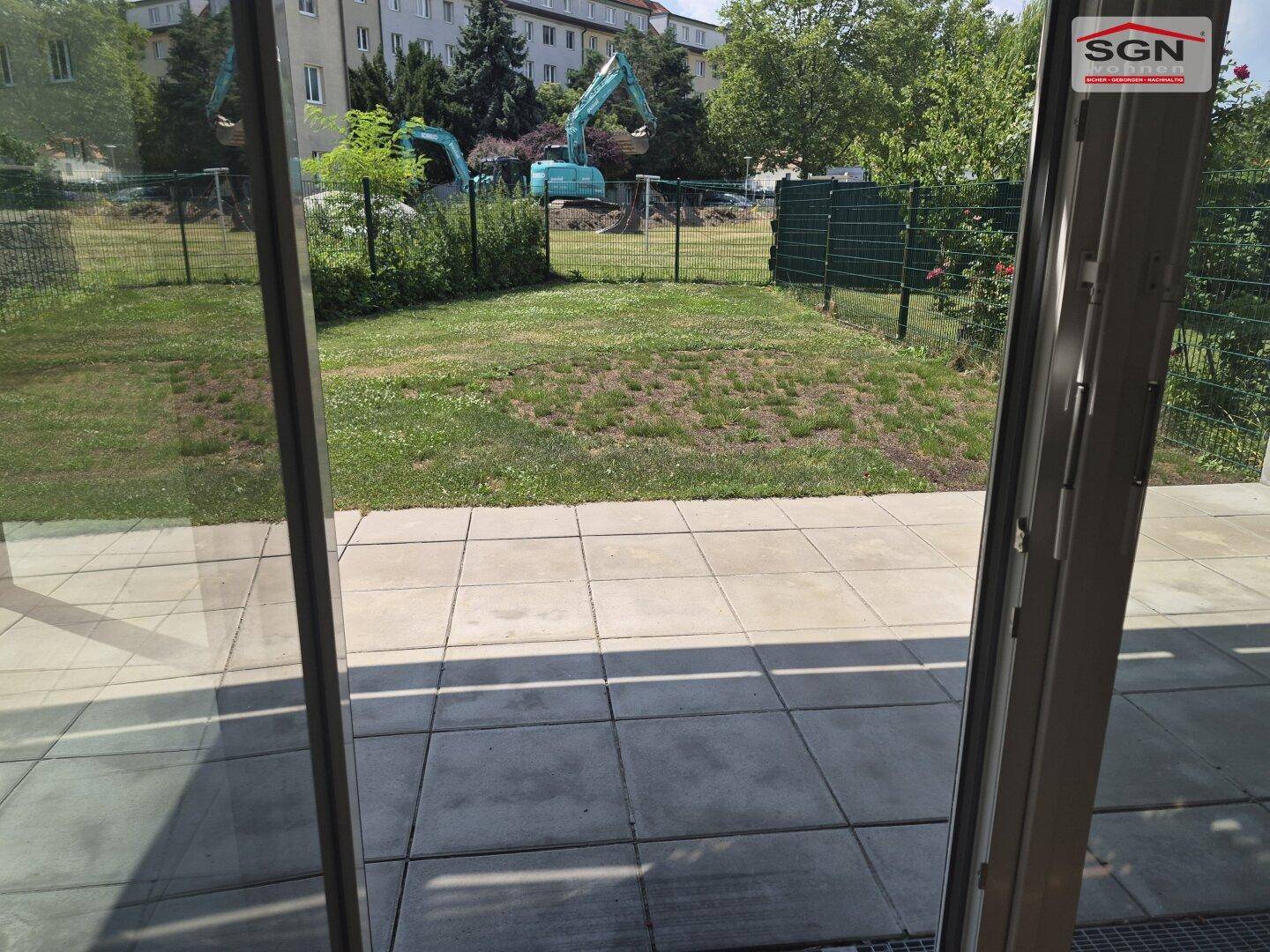 Blick von der Terrasse auf den Garten mit Rasenfläche und angrenzender Baustelle.