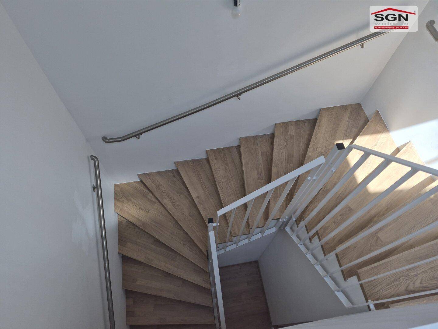 Moderne Holztreppe mit weißem Geländer, die die Stockwerke des Hauses verbindet.