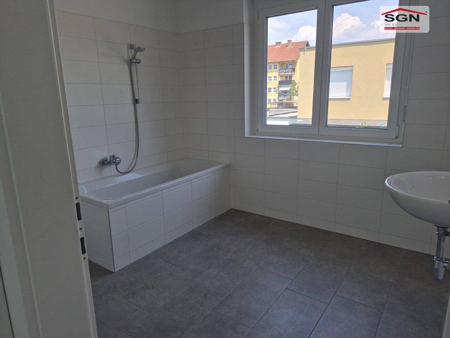 Helles Badezimmer mit Badewanne, Waschbecken und Fenster mit Blick nach draußen.