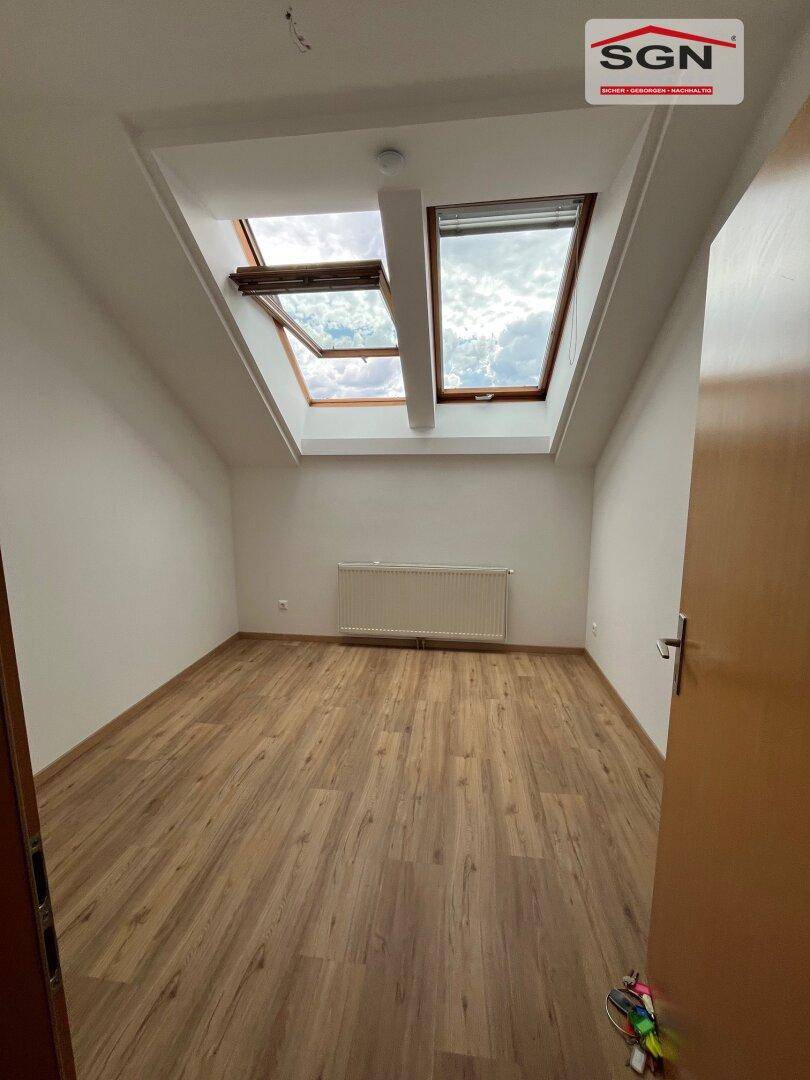 Schlafzimmer mit Holzboden, Dachschrägen und zwei großen Dachfenstern für viel Tageslicht.