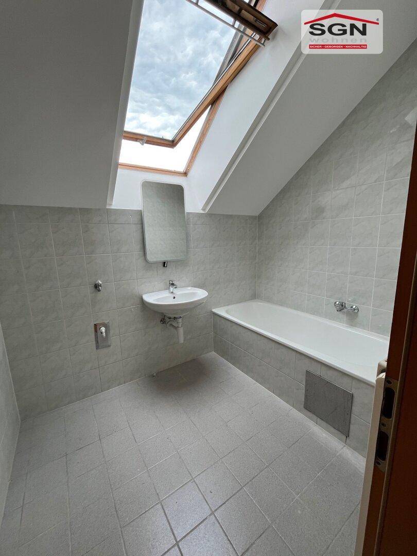 Badezimmer mit Badewanne, Waschbecken, Fliesenboden und einem Dachfenster für natürliche Belüftung.