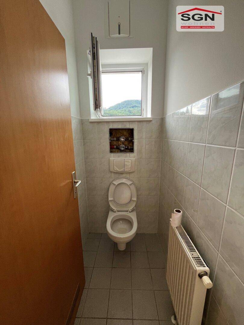 Separates WC mit Toilette, kleinem Fenster und Fliesen an Wänden und Boden.