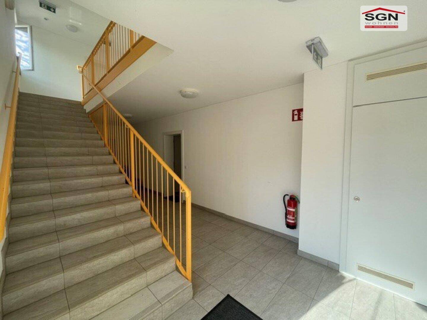 Heller Treppenaufgang in einem Mehrfamilienhaus mit Fliesenboden und gelbem Geländer.