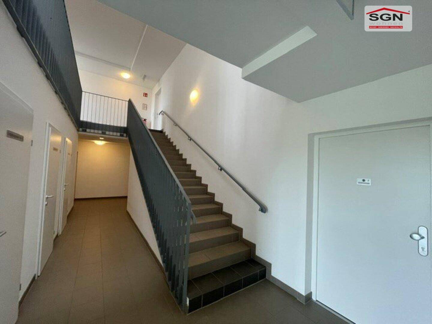 Helles Treppenhaus mit Fliesenboden und Zugang zu mehreren Wohneinheiten in einem modernen Gebäude.