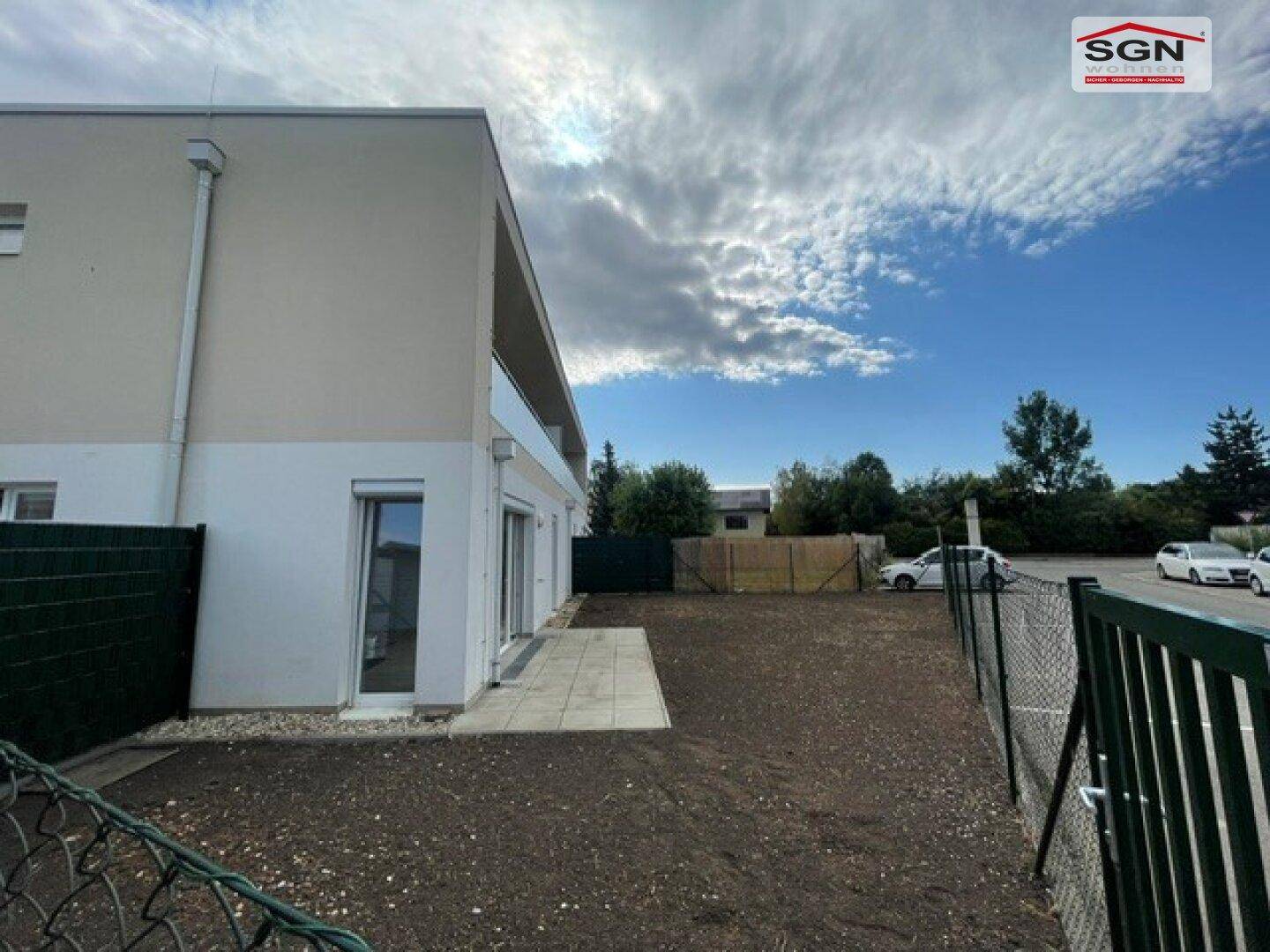 Gebäudeseite mit kleiner gepflasterter Terrasse und angrenzendem, eingezäuntem Gartenbereich.