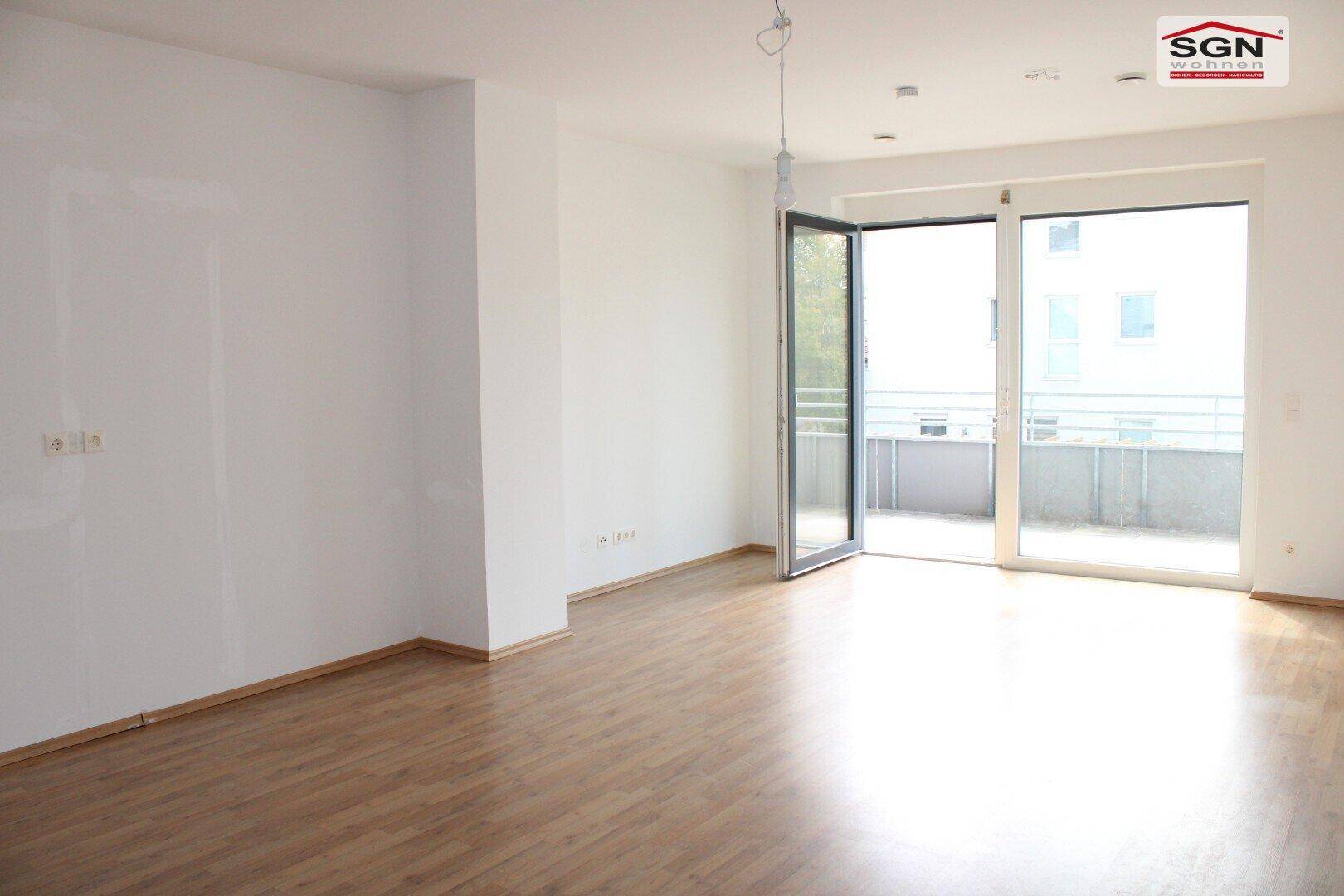 Helles, leeres Zimmer mit Holzboden und Zugang zu einem Balkon, ideal für einen Wohnbereich.