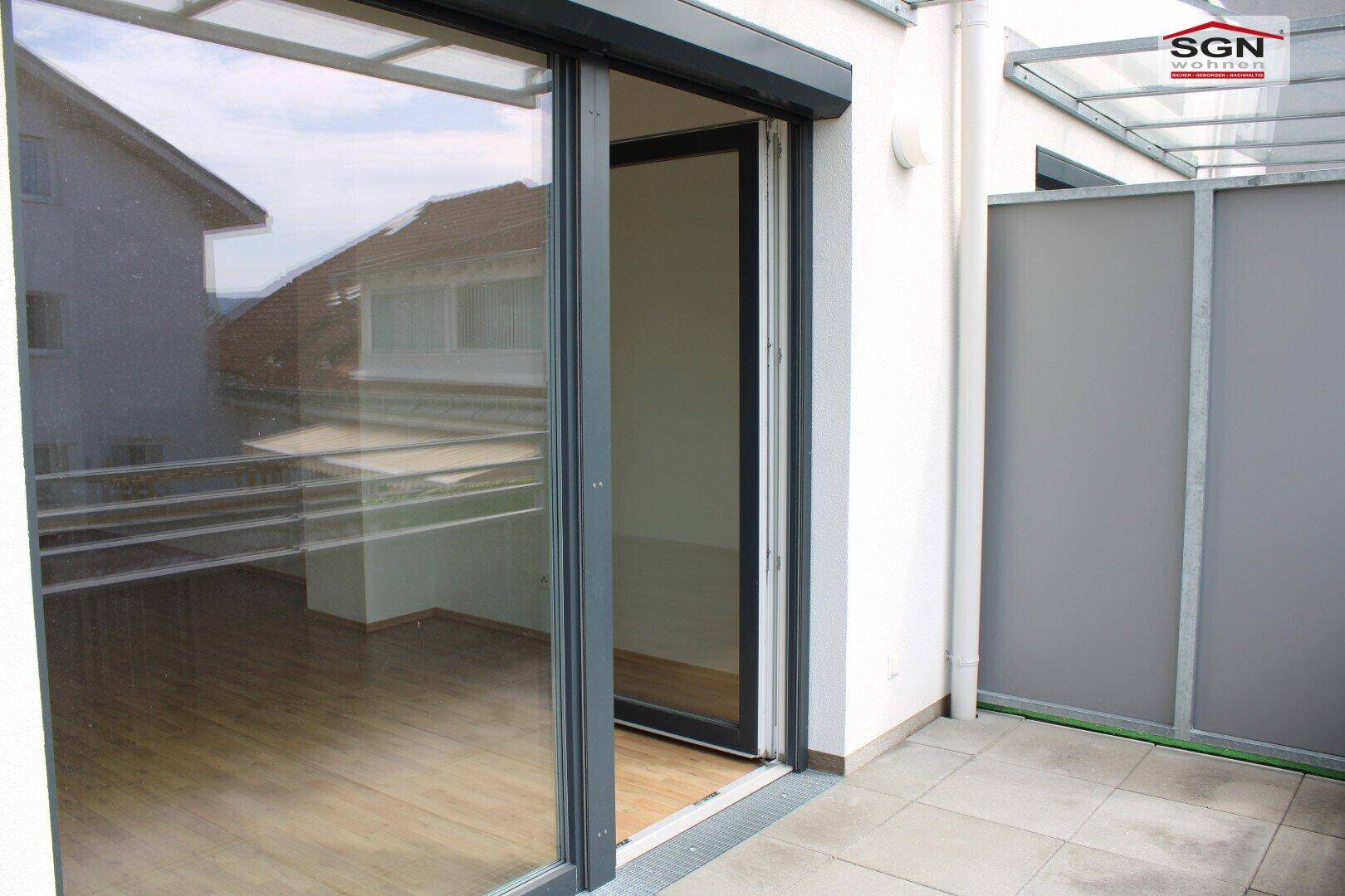 Terrasse mit großzügiger Glasschiebetür, die den Blick in einen hellen Innenraum freigibt.