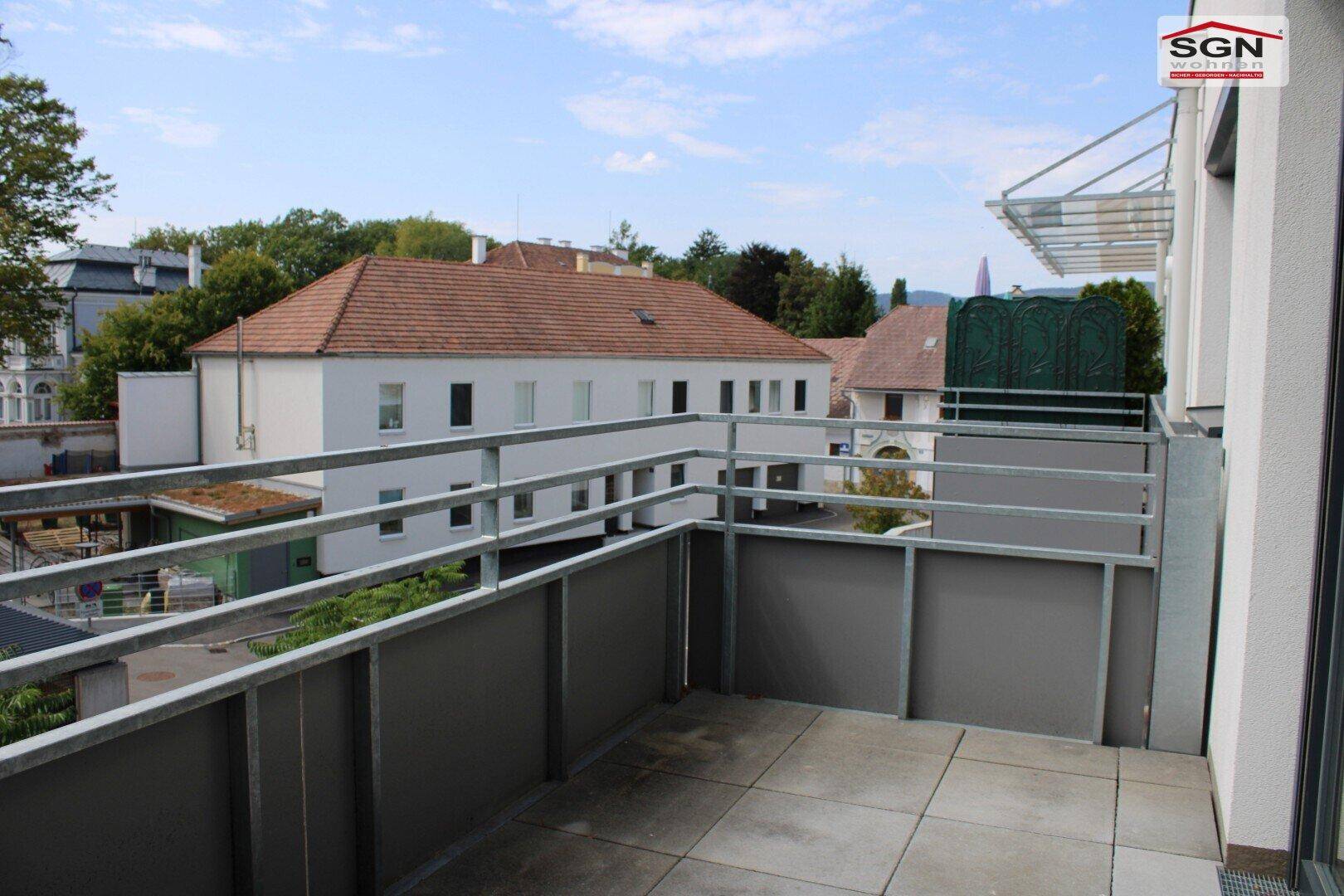 Geräumiger Balkon mit Metallgeländer und Blick auf umliegende Gebäude und Grünflächen.