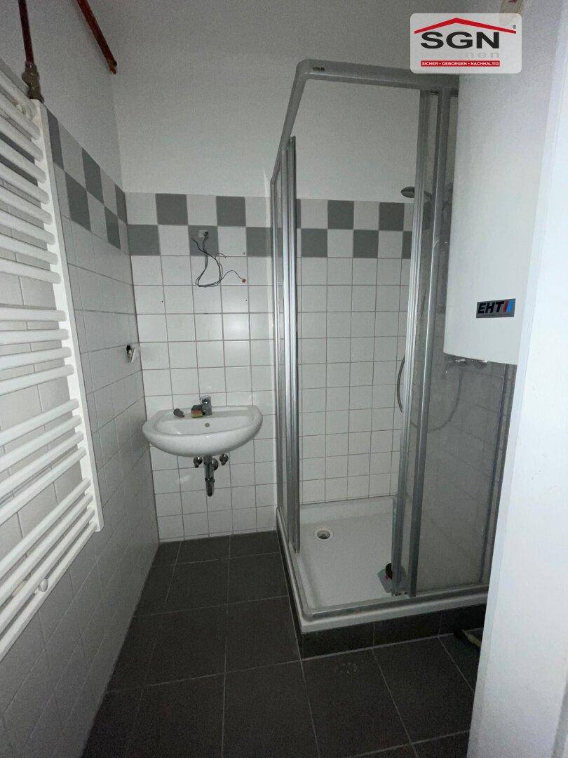 Badezimmer mit Duschkabine, Waschbecken und weiß-grauen Fliesen an den Wänden, inklusive Handtuchheizkörper.