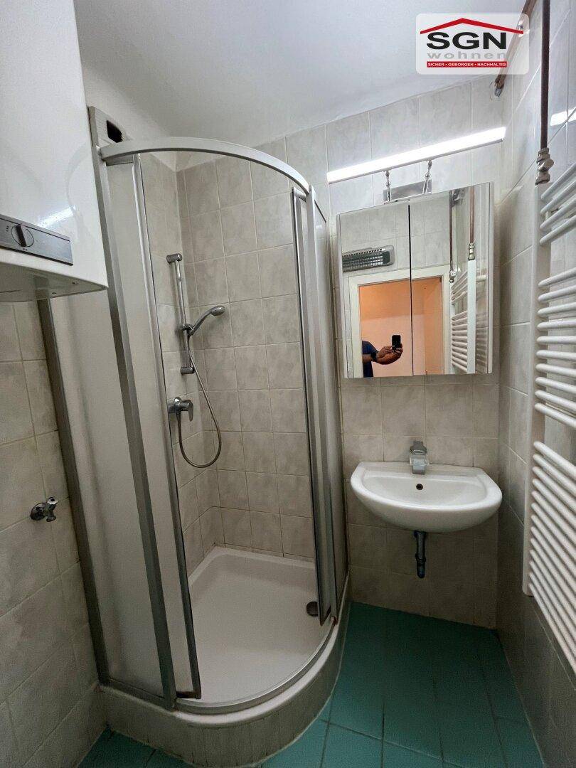 Kleines Badezimmer mit Duschkabine, Waschbecken und Spiegelschrank, hell gefliest.