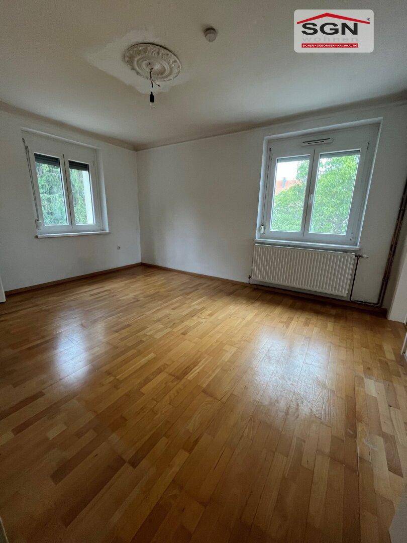 Helles Zimmer mit Parkettboden, zwei Fenstern und Stuckdecke, bietet viel Tageslicht.