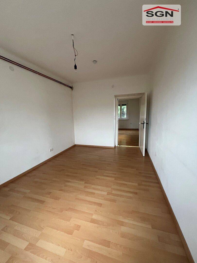 Leeres Zimmer mit Laminatboden und Zugang zu einem weiteren Raum, bietet viel Potenzial.