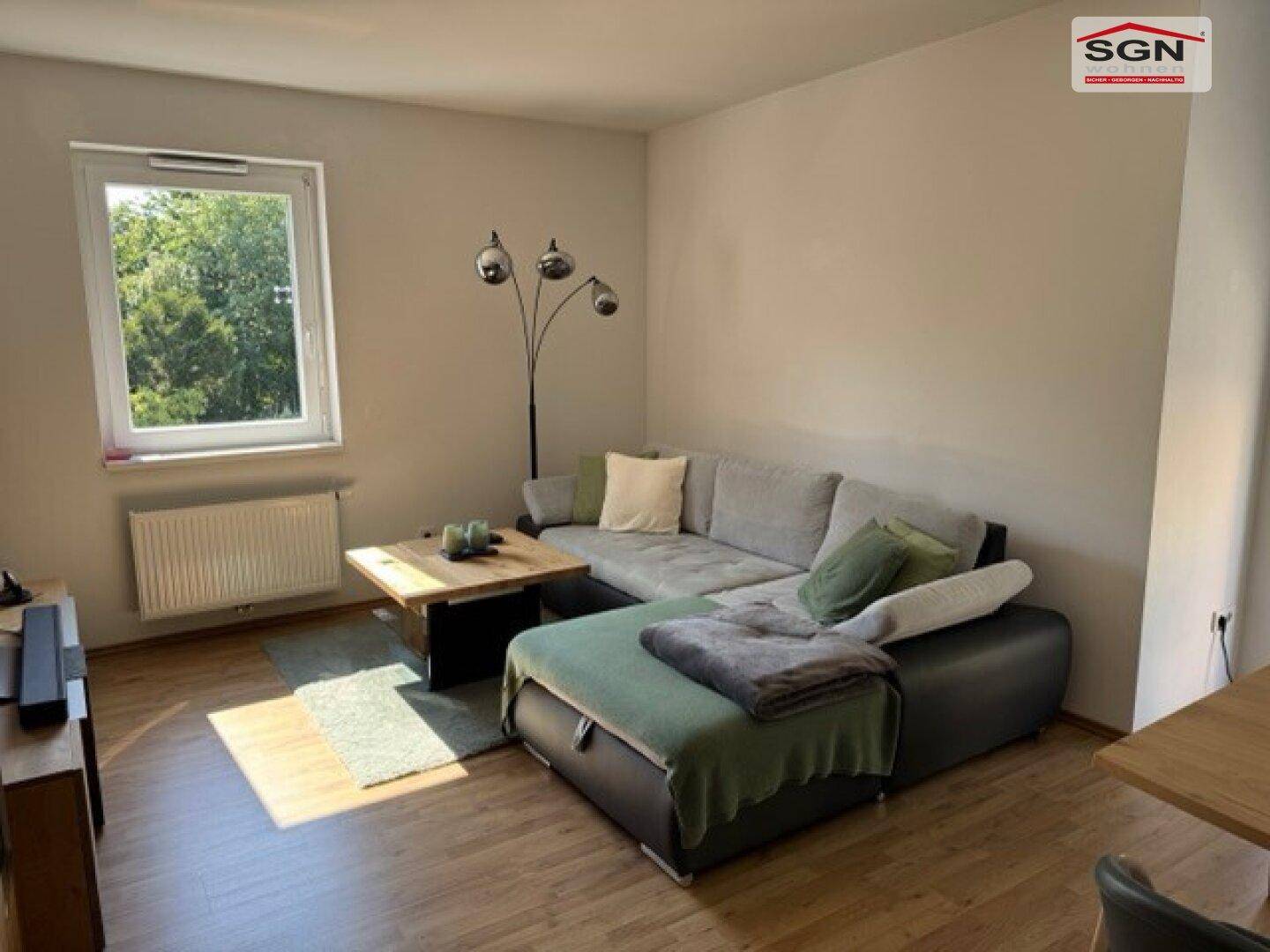 Gemütliches Wohnzimmer mit Sofa, Couchtisch und Fenster mit Blick ins Grüne.