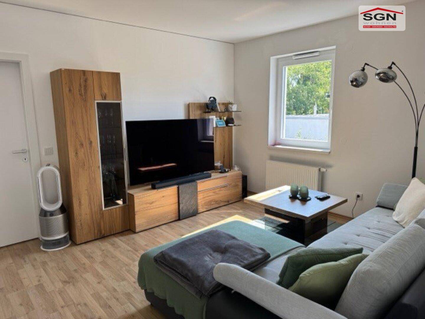 Wohnzimmer mit TV-Möbeln aus Holz, Sofa und Fenster, das viel Tageslicht hereinlässt.
