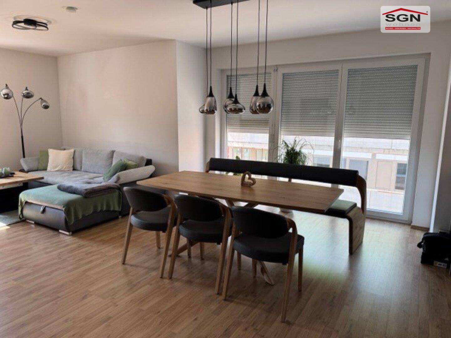 Heller Wohn- und Essbereich mit Holzboden, großem Esstisch und Zugang zum Balkon.