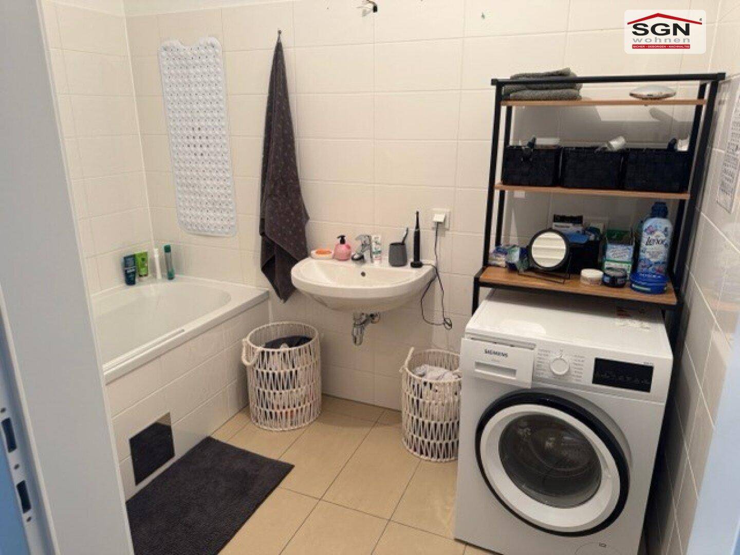 Badezimmer mit Badewanne, Waschbecken, Waschmaschine und hellen Wand- und Bodenfliesen.