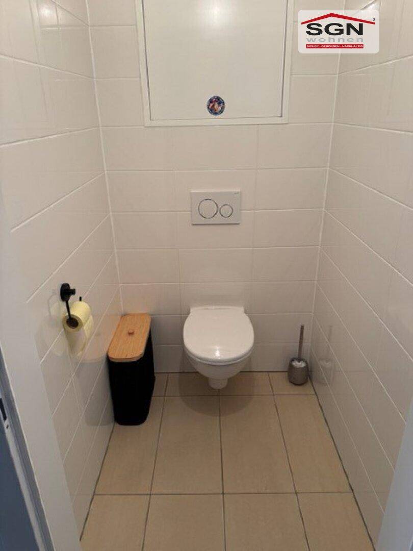 Kleines Gäste-WC mit weißen Fliesen, wandhängendem WC und hellem Fliesenboden.