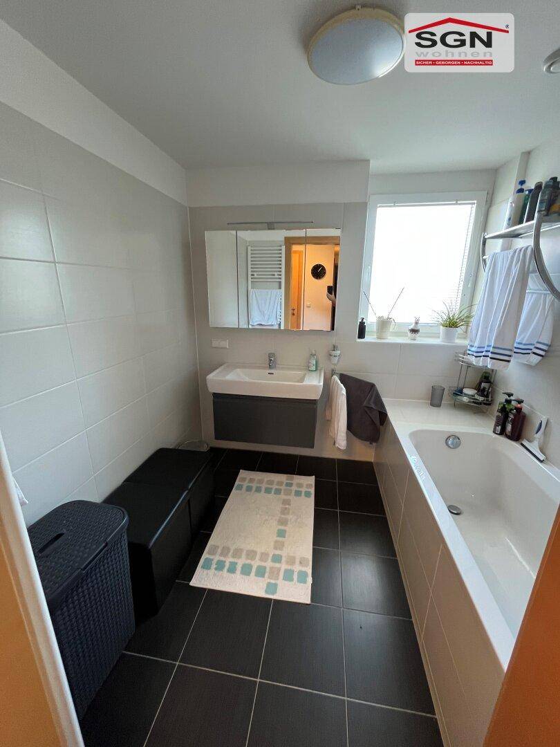 Helles Badezimmer mit Badewanne, modernem Waschtisch und grauen Fliesen.
