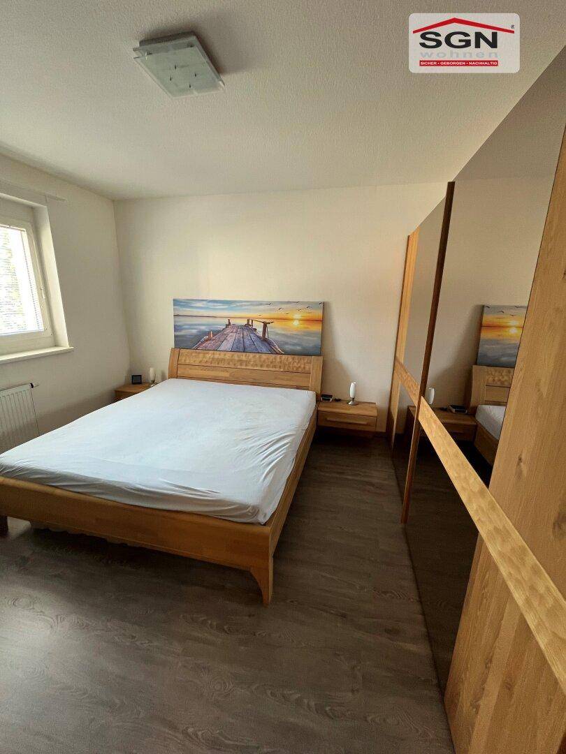 Schlafzimmer mit hellem Holzbett, Nachttischen und großem Spiegelschrank.