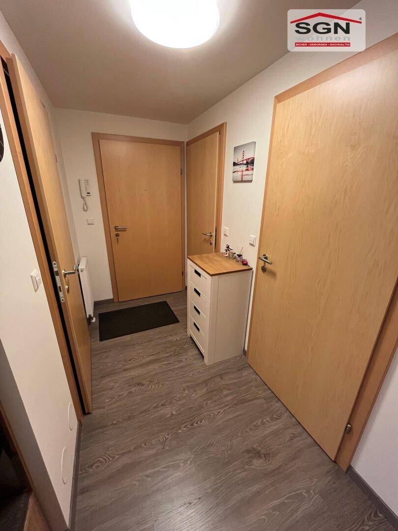 Eingangsbereich mit Laminatboden, mehreren Holztüren und einer kleinen Kommode.