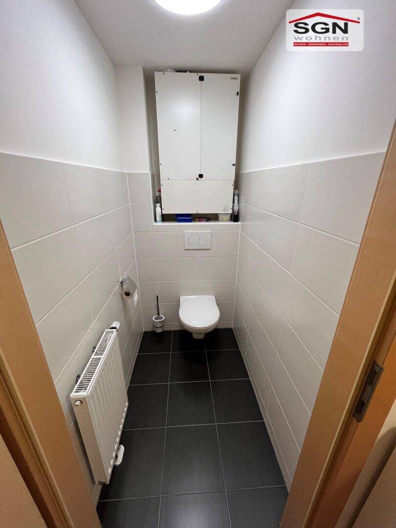 Kleines Gäste-WC mit Wand-WC, Heizkörper und weißen sowie dunklen Fliesen.