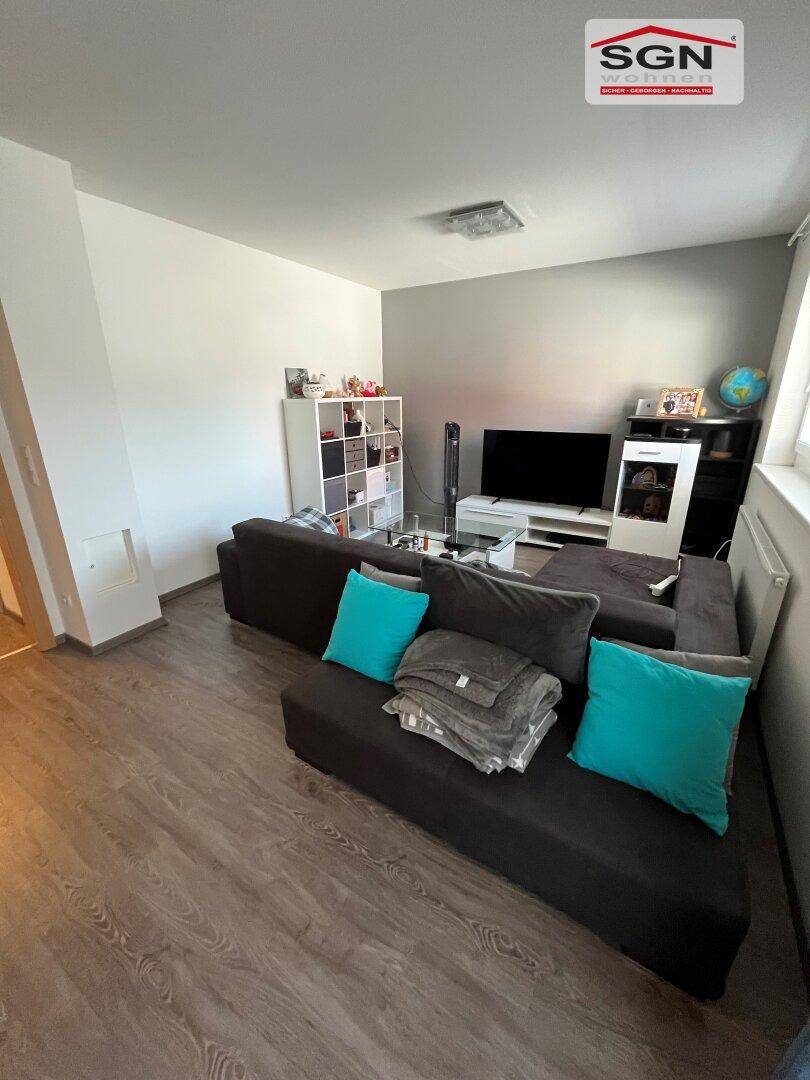 Helles Wohnzimmer mit grauem Ecksofa, Regalen und Laminatboden.