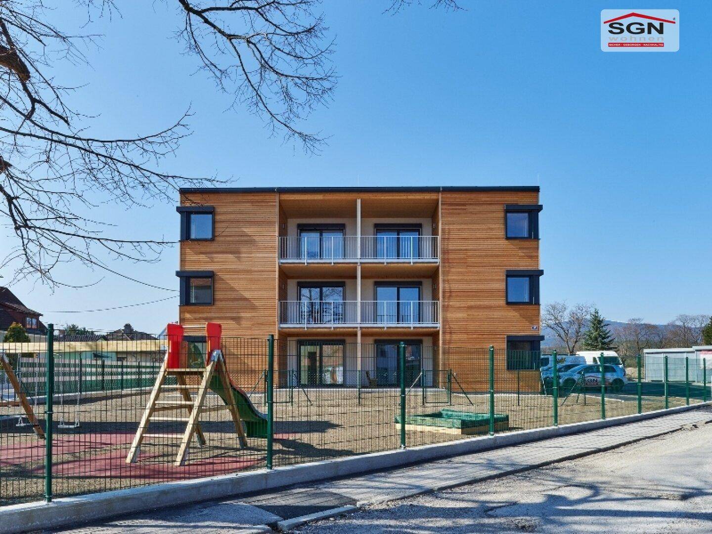 Rückseite der modernen Wohnanlage mit Balkonen und einem Kinderspielplatz im Vordergrund.
