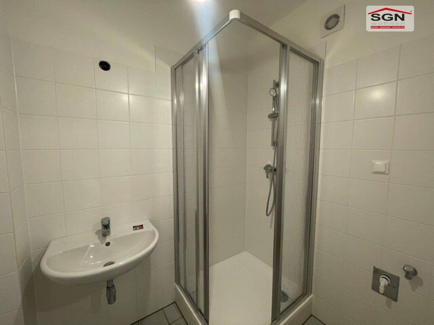 Funktionales Badezimmer mit Duschkabine, Waschbecken und weißen Fliesen.